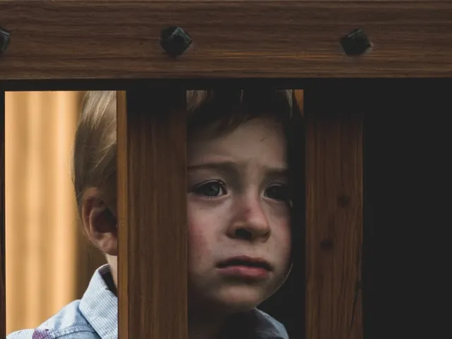 Sad young boy looking out between the wooden bars of a railing